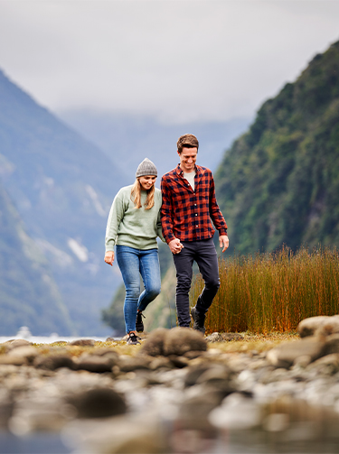 Young couple walking holding hands in Milford sounds smiling whilst talking about the success of their investment funds